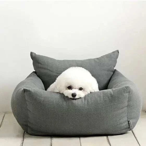 Small white fluffy dog resting in a gray portable car dog bed for travel and indoor comfort